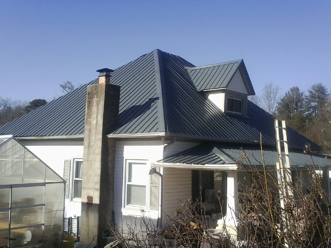 Dark blue standing seam metal roof on a white farmhouse with dormer — Slate & Tile Roof Repair by Roofing Brothers in Yellow Pine