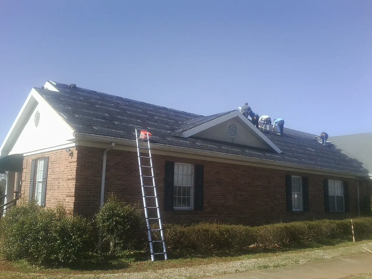 Crew tearing shingles off a brick ranch roof with a ladder set — Metal Roof Repair work by our crew in Yellow Pine