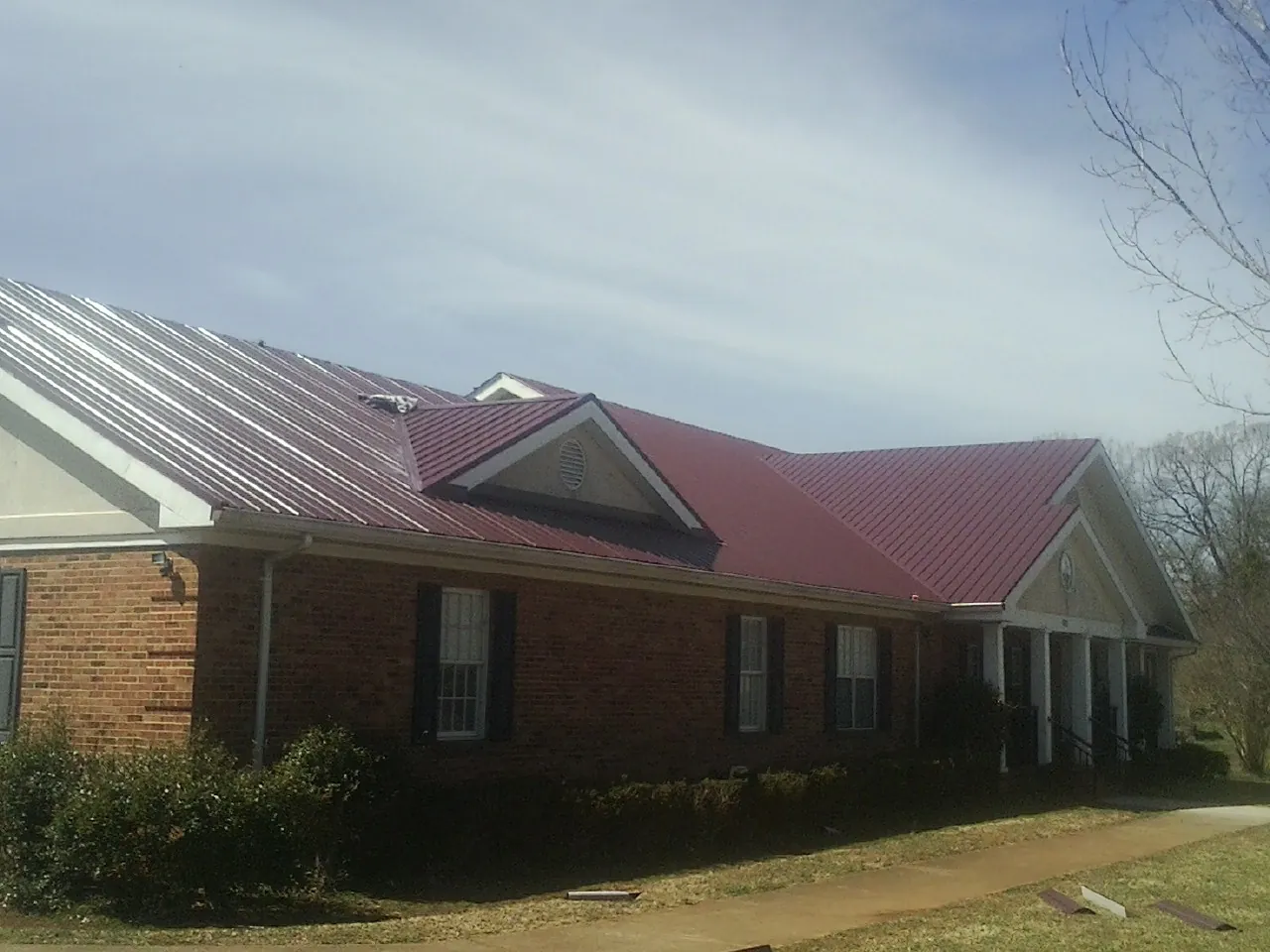 Red metal roof with gabled entries on a long brick building, from a Hail Damage Roof Repair job in Yellow Pine