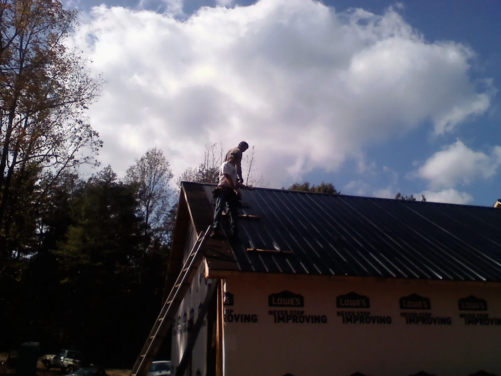 Roofer fastening dark metal panels high against a cloudy sky, from a Roof Inspection job in Yellow Pine
