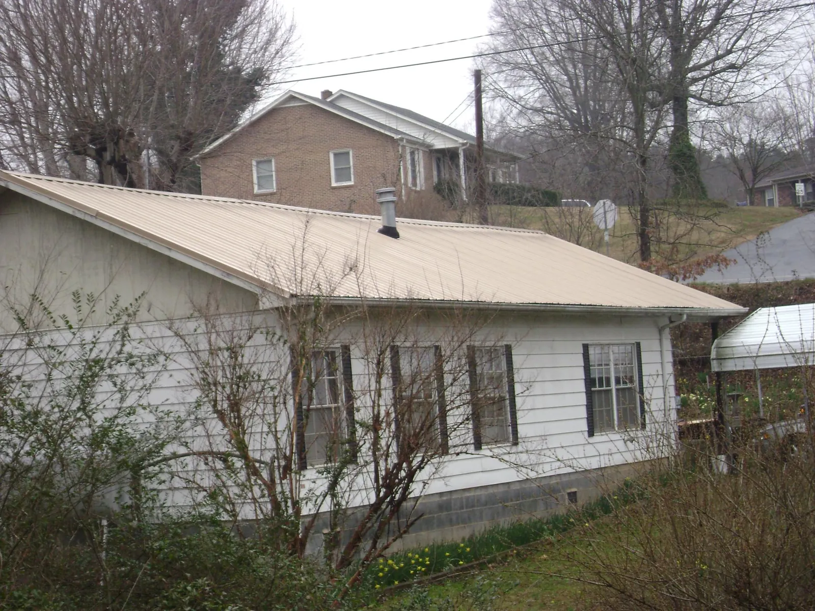 Tan metal roof on a white sided house set into a hillside — Commercial Roofing by Roofing Brothers in Yellow Pine